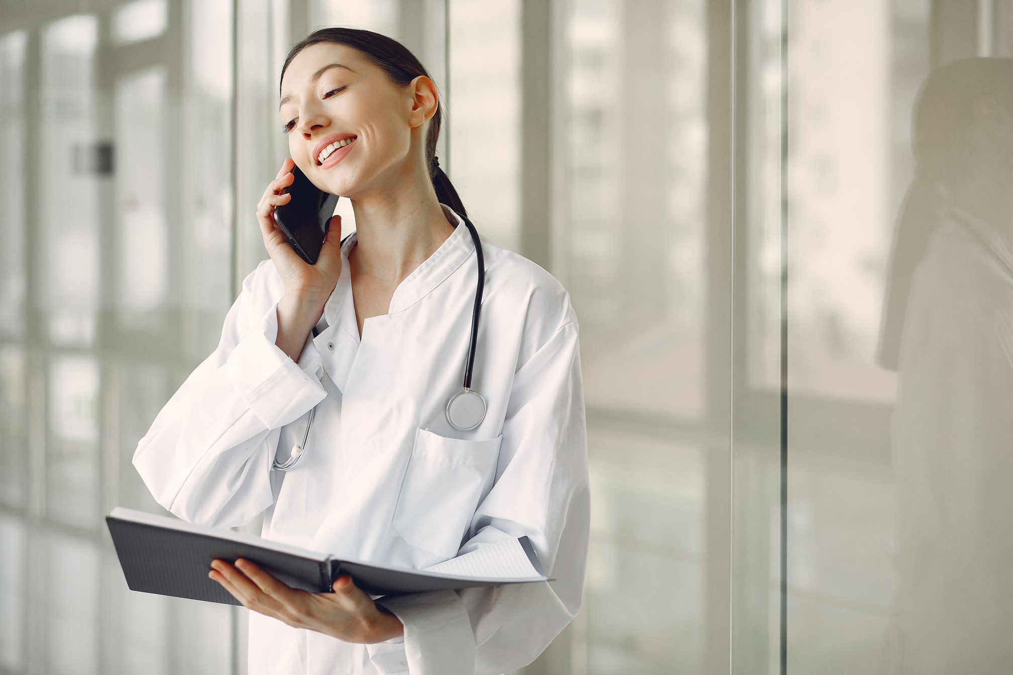 Positive doctor in uniform with stethoscope and documents talking on smartphone